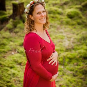 schwangerschaftsshooting mit rotem kleid im wald vor moos mit blumenkranz im winter in hoechstadt an der aisch